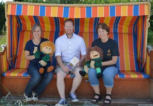 Drei Menschen mit zwei Handpuppen in einem bunten Strandkorb