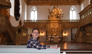 Ein Mann sitzt in einer Kirchenbank, im Hintergrund ein Altarraum